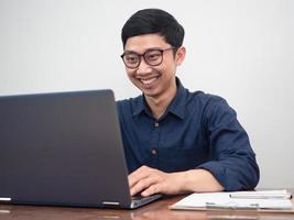 zakenman slijtage bril gelukkig met werken gebruik makend van laptop Bij werkplaats tafel foto