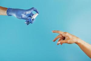 de hand- is uitgebreid naar de gehandschoende hand- en de antiseptisch verstuiven in de blauw handschoen Aan een blauw achtergrond. foto