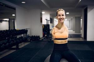 gelukkig zonder armen vrouw atleet ontspannende Aan geschiktheid bal in een Sportschool en op zoek Bij camera. foto