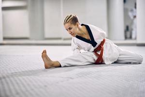 zonder armen atletisch vrouw aan het doen uitrekken opdrachten Aan de verdieping gedurende taekwondo opleiding. foto