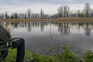 een Mens is zittend Aan de oever van de rivier visvangst met visvangst staven. foto