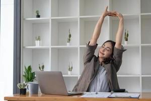 Aziatisch zakenvrouw strekt zich uit haar armen naar kom tot rust haar moe spieren van werken Bij haar bureau allemaal dag Bij de kantoor. foto