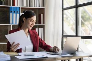 glimlach mooi bedrijf Aziatisch vrouw is werken haar baan Aan een laptop computer in een modern kantoor. aan het doen accounting analyse verslag doen van echt landgoed investering gegevens, financieel en belasting systemen concept foto