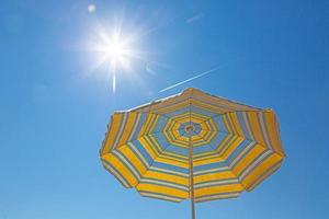 beeld van geel blauw gekleurde parasol in voorkant van helder blauw lucht foto