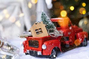 rood retro auto met een Kerstmis boom siert met de huis sleutel in de oppakken vrachtauto voor kerstmis. buying een huis, in beweging, hypotheek, lening, echt landgoed, feestelijk stemming, nieuw jaar foto