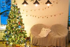 Kerstmis boom in wit interieur van een huis met loft-stijl steen muren met slingers van glas speelgoed Aan een touw. gloeiend fee lichten decoratie van de studio kamer. knus huis in Kerstmis en nieuw jaar foto