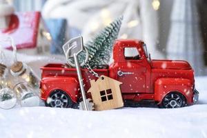 rood retro auto met een Kerstmis boom siert met de huis sleutel in de oppakken vrachtauto voor kerstmis. buying een huis, in beweging, hypotheek, lening, echt landgoed, feestelijk stemming, nieuw jaar foto