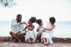 gelukkig Afrikaanse Amerikaans familie, vader, moeder, twee dochter genieten van samen Aan park kust. foto