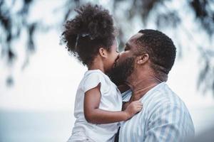 Afrikaanse Amerikaans vader draag- dochter en kusjes Aan wang met vrolijk liefdevol. gelukkig familie. foto
