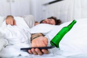 sms'en terwijl dronken concept. jong Mens aan het liegen in bed dodelijk dronken Holding leeg fles van drank. dronken met alcohol . alcoholisme gewoonte dronkenschap schadelijk gewoonte concept foto