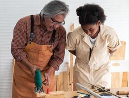 tiener meisjes leren naar gebruik een elektronisch zag en Speel met hun opa in de houten werkplaats, een concept voor verbeteren de ontwikkeling en denken van kinderen. foto