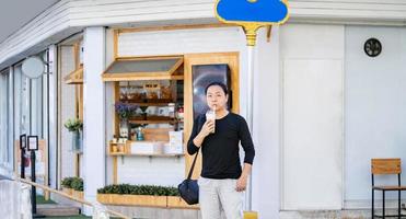 Aziatisch Mens in de zwart t-shirt houdt de bubbel bal ijs melk thee in voorkant van de winkel Aan de buitenshuis straat voetpad. foto