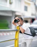 professioneel Aziatisch camera Mens focus Aan de beeld met zijn spiegelloos camera naast de straat buitenshuis veld. foto