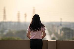 Aziatisch vrouw tiener staat achterkant in voorkant van stad visie Bij op het dak van de gebouw foto