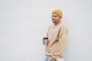 portret van elegant Mens hipster in geel hoed met papier kop van koffie Bij de stad foto