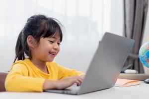 eerste dag Bij school. Aziatisch weinig meisje gebruik makend van een laptop computer, aan het studeren door online e-learning systeem. foto