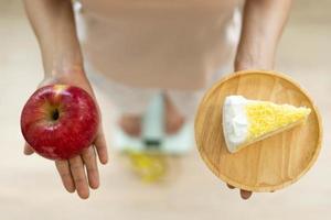 Dames zijn kiezen de Rechtsaf voedsel voor mooi zo Gezondheid. Dames zijn vasten. vergelijking opties tussen donuts en appels gedurende gewicht meting Aan digitaal schubben. eetpatroon concept. foto