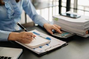 zakenvrouw of accountant hand- schrijven Aan de kladblok werken naar berekenen Aan bureau over kosten Bij kantoor. foto