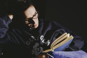 vrouw ontspannende Aan sofa en lezing boek. avond humeurig sfeer. ze is genieten van tijd gedurende weekend foto