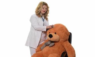 dichtbij omhoog van jong vrouw dokter in uniform controle teddy beer met stethoscoop Bij kliniek. zelfverzekerd medisch beoefenaar of gezondheidszorg arbeider onderzoeken teddy beer Bij ziekenhuis foto