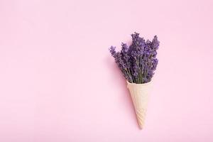 lavendel bloemen boeket in een wafel ijshoorntje Aan een gekleurde achtergrond. minimaal zomer of voorjaar concept foto
