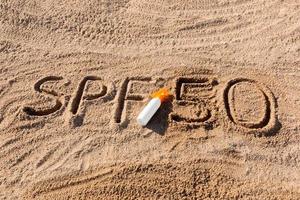 zon beschermen factor vijftig. spf 50 woord geschreven Aan de zand en wit fles met zonnebrand room. huid zorg concept achtergrond foto
