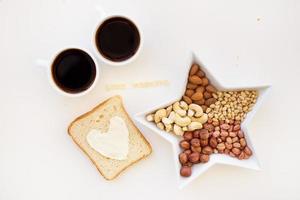 belegd broodje voor ontbijt in het formulier van hart met kaas, een kom van noten en mengen twee cups van koffie, mooi zo ochtend- opschrift foto