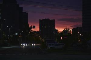 roze helder zonsondergang en auto's Aan de weg. daken van huizen en een helder zonsondergang. foto