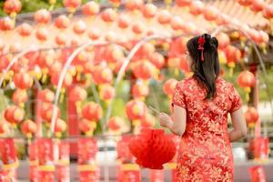 jong Aziatisch vrouw vervelend traditioneel cheongsam qipao jurk Holding lantaarn en staand met haar terug terwijl bezoekende de Chinese boeddhistisch tempel. vieren Chinese maan- nieuw jaar. foto