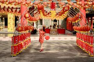 mooi jong Aziatisch vrouw vervelend traditioneel cheongsam qipao jurk Holding lantaarn en wandelen terwijl bezoekende de Chinese boeddhistisch tempel. vieren Chinese maan- nieuw jaar, feestelijk seizoen vakantie. foto