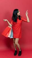 mooi vrouw vervelend traditioneel cheongsam qipao jurk Holding boodschappen doen zak en hand- richten geïsoleerd Aan rood achtergrond. gelukkig Chinese nieuw jaar foto