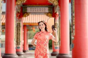 gelukkig Chinese nieuw jaar. mooi Aziatisch vrouw vervelend traditioneel cheongsam qipao jurk Holding ventilator terwijl bezoekende de Chinese boeddhistisch tempel. emotie glimlach foto