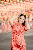 verticaal afbeelding. gelukkig Chinese nieuw jaar. Aziatisch vrouw vervelend traditioneel cheongsam qipao jurk poseren konijn in Chinese boeddhistisch tempel. vieren Chinese maan- nieuw jaar, feestelijk seizoen vakantie. foto