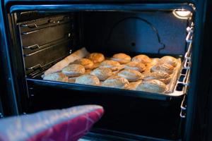 menselijk hand- met een oven handschoen nemen uit van de oven een dienblad met gebakje knoedels foto