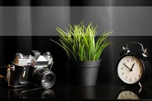 dichtbij omhoog visie van werk tafel met camera, klok en kamerplant Aan zwart tafel. hoog kwaliteit foto