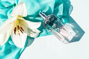 kunstmatig parfum verstuiven in een glas transparant fles Aan een licht achtergrond met een lelie bloem en een vrouw sjaal. de concept van schoonheid. foto