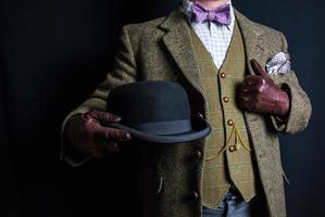 portret van Mens in tweed pak Holding bowler hoed Aan zwart achtergrond. wijnoogst stijl en retro mode van Engels heer. foto