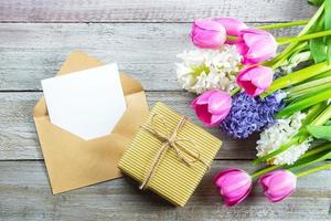 mockup moeder dag concept. voorjaar bloemen tulpen en hyacint, geschenk doos en leeg kaart Aan haveloos houten achtergrond. groet kaart voor vrouwen of moeders dag. vlak leggen, top visie, kopiëren ruimte. foto