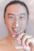 jong Aziatisch Mens Holding injectie met vulmiddel in voorkant van zijn gezicht. Aziatisch Mens in schoonheid salon. plastic chirurgie kliniek. foto