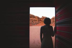 vrouw persoon staan in woestijn bedoeïenen kamp binnen traditioneel tent met Open deur genieten wadi rum woestijn kliffen en texturen vroeg ochtend- foto