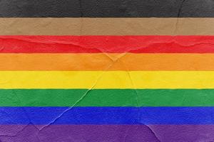 trots regenboog vlag met zwart en bruin strepen geschilderd Aan gebarsten getextureerde muur. buitenshuis grunge structuur achtergrond foto