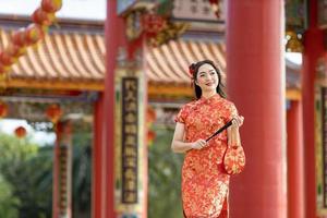 Aziatisch vrouw in rood cheongsam qipao jurk Holding papier ventilator terwijl bezoekende de Chinese boeddhistisch tempel gedurende maan- nieuw jaar voor traditioneel cultuur concept foto