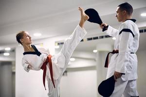 vastbesloten krijgshaftig kunstzinnig met onbekwaamheid oefenen hoog been trap met haar trainer gedurende taekwondo opleiding. foto