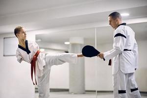 gemotiveerd atletisch vrouw met een onbekwaamheid beoefenen been trap met taekwondo trainer in Gezondheid club. foto