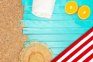 strand indeling. kiezelsteen zand met een azuur horizontaal houten pier of zon ligstoel. rietje hoed, handdoek en geel sinaasappelen. reizen en toerisme. kopiëren ruimte foto