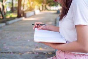 een jong vrouw hand- door schrijven een pen Aan een park notitieboekje in de avond. foto