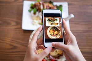 vrouw gebruik makend van mobiel telefoon naar nemen afbeeldingen van voedsel Aan de tafel. genomen Aan mobiel en zetten Aan sociaal netwerken. foto