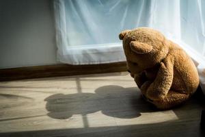 de teddy beer keek verdrietig en teleurgesteld zittend in de hoek van de kamer. de teddy beer lijkt eenzaam in een kamer met zonlicht. concept depressie in kinderen foto