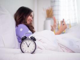 de focus beeld Aan de klok en achtergrond hebben de meisje is gebruik makend van een mobiel telefoon naar babbelen met een video telefoontje met haar vriendje in de slaapkamer en slaap heel laat. foto