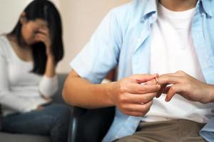 de jong Mens is Verwijderen de bruiloft ring van zijn vinger. de terug is een jong vrouw zittend in voorkant van haar schreeuw. familie problemen foto